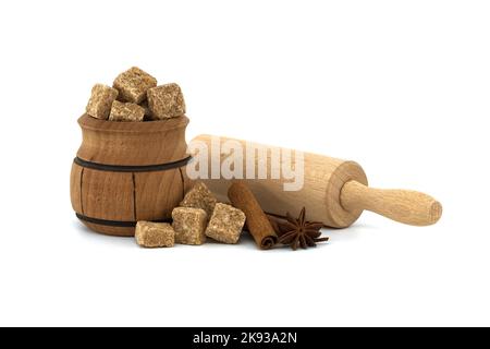Brown cane sugar cubes in wooden sugar bowl next to cinnamon sticks, star anise and rolling pin. Confectionery concept isolated on white background Stock Photo