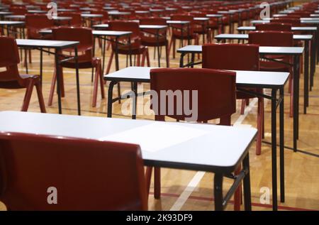 A large high school hall filled with multiple exam tables and red chairs set up organized and ready for an major exams or student testing.  Rows of ex Stock Photo