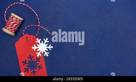 red gift tag with snowflakes and red and white thread on spool. dark blue background. Stock Photo