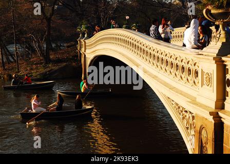 People enjoy a beautiful and warm early spring day, rowing on the lake or simply walking across the Bow Bridge in New York City's Central Park Stock Photo