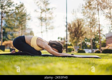 Side view of a woman in comfy activewear, resting performing relaxation exercise, and stretching lower back. Outdoor lifestyle. Healthy lifestyle Stock Photo