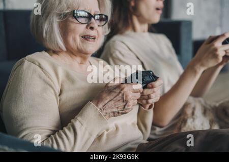 Happy family of two members resting on sofa at home with joysticks, playing games on video console. Lying on comfortable sofa, playing online games Stock Photo