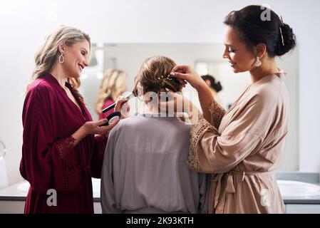 We wanna make sure you look perfect. two attractive young bridesmaids doing the brides hair and make-up in preparation of her wedding. Stock Photo