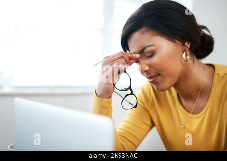 My head is aching. an attractive young woman sitting in her home and suffering from a headache while using her laptop. Stock Photo