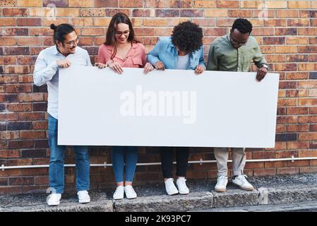 Everyones talking about this. a group of young people holding a blank banner against an urban background outdoors. Stock Photo