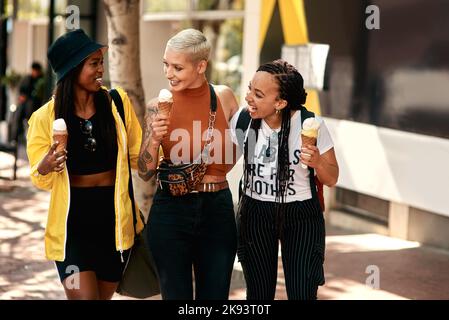 We love spending time together. three friends enjoying ice cream cones while out in the city. Stock Photo
