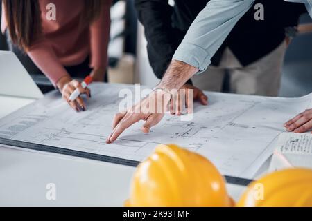 We need to pay careful attention to this area. three unrecognizable architects going over blueprints and building plans together in their office. Stock Photo