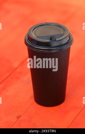 Disposable black plastic coffee cup on red wooden table Stock Photo