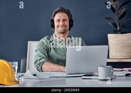 Everything is working in my favor today. Portrait of a handsome young architect wearing headphones while working in his office. Stock Photo