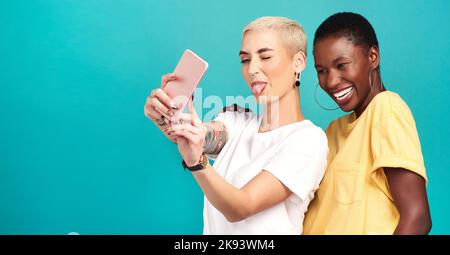 Selfies are better when we take them together. Studio shot of two young women taking selfies together against a turquoise background. Stock Photo