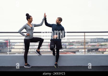 Being active together means staying happy together. a sporty young man and woman giving each other a high five while exercising outdoors. Stock Photo