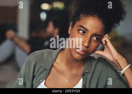 Sometimes love just isnt enough. an attractive young woman looking upset while her boyfriend sits in the background at home. Stock Photo