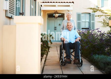 Rolling around with my love. Full length shot of a cheerful wheelchair bound senior man relaxing with his wife in their backyard at home. Stock Photo