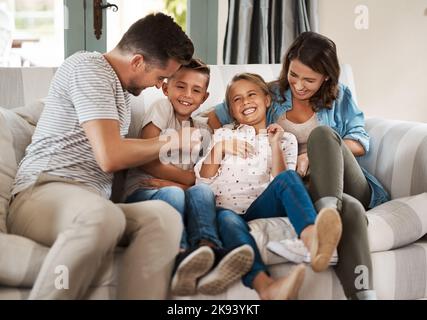 Tickles and giggles put the heart into a home. a happy young family of four playing together on the sofa at home. Stock Photo