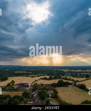 Stunning aerial landscape image of the sun’s rays shining through gap in clouds onto English countryside captured by drone in portrait mode Stock Photo