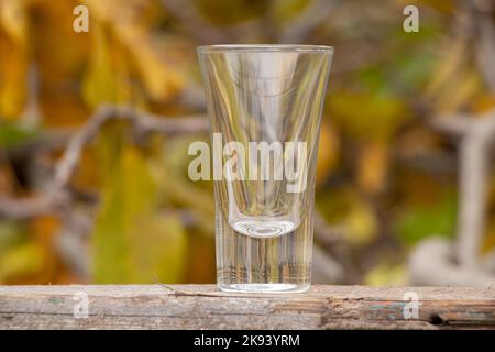 empty glass goblet for alcoholic beverages stands on a wooden table in yellow leaves in the autumn on the street Stock Photo