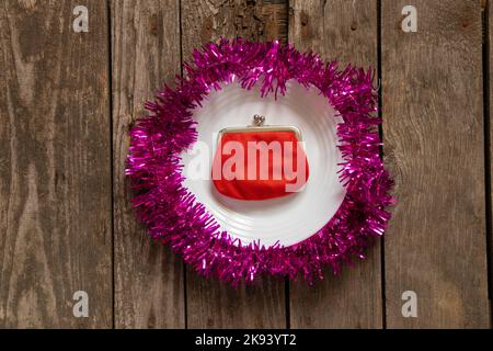 red wallet lies on a white plate decorated New Year's colored ribbon on a wooden background close-up, New Year's decor Stock Photo