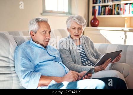 Getting to grips with smart gadgets in their golden years. a senior couple using their smart devices on the sofa at home. Stock Photo