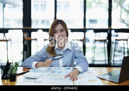 Financial analysts analyzing business financial reports are examining documents using a magnifying glass as a working concept Stock Photo