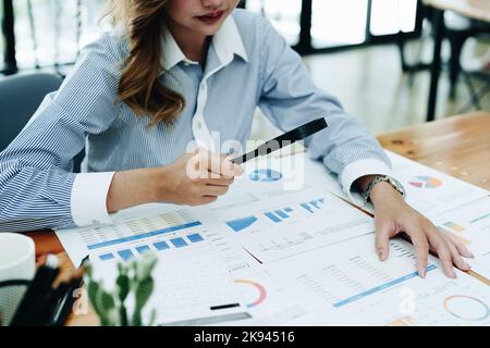 Financial analysts analyzing business financial reports are examining documents using a magnifying glass as a working concept Stock Photo