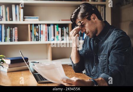 All this paperwork is giving me a headache. a young businessman looking stressed out while working on a laptop in his office at home. Stock Photo