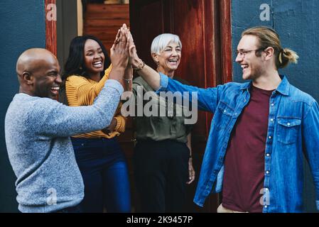 Weve all got that winners mentality. a group of businesspeople joining together for a high five while standing outside their office building. Stock Photo