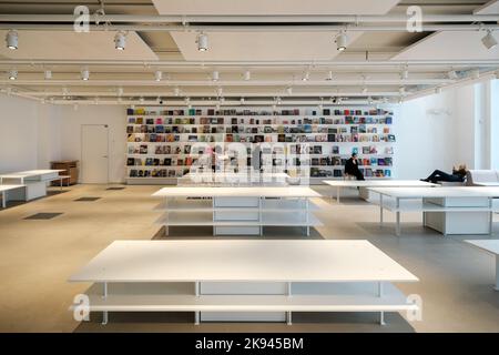 Vilnius, Lithuania - Octobe 10, 2022: Students examining books on bookcase and taking photo behind tables in light modern library in daytime Stock Photo
