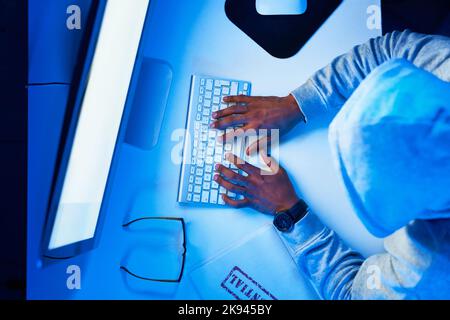 Hes on top of the cyber criminal world. High angle shot of a young male hacker cracking a computer code in the dark. Stock Photo