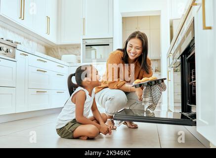 Asian, mom and girl in kitchen at oven, baking and cupcakes with stove, happy and home. Mother, child and muffins for learning, education and cooking Stock Photo