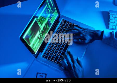 He can crack through any system. High angle shot of an unrecognizable hacker using a laptop in the dark. Stock Photo