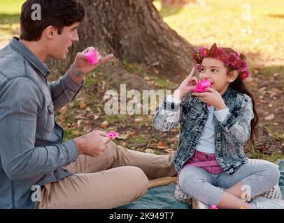 The tea is absolutely divine mlady. an adorable little girl having a tea party in the park with her father. Stock Photo