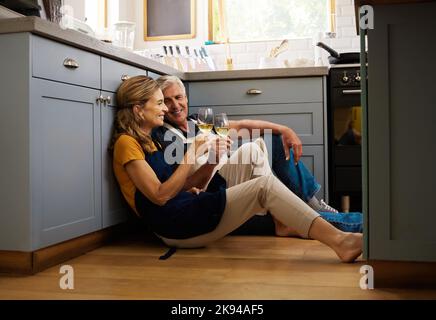 Love, senior couple and on kitchen floor, together and bonding while speaking, talking and with wine. Romantic, retirement or elderly man and woman Stock Photo