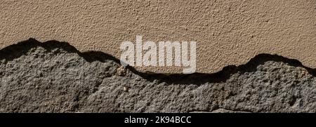 Old sandstone wall with thick pieces of plaster broken off Stock Photo