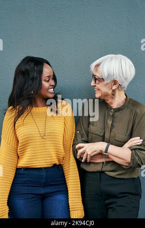 Were always on the same page. two cheerful businesswomen having a discussion while standing against a wall outdoors. Stock Photo