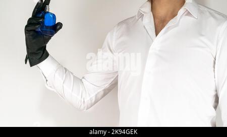 White shirt man spray perfume with hand. Blue bottle and leather black gloves on white background. Men sprey parfume or eau de cologne smell great. Stock Photo