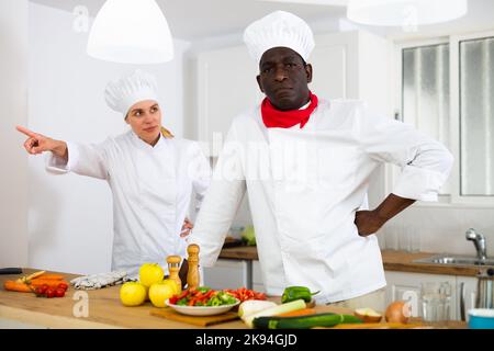 Strict female chef reprimanding male colleague in private kitchen Stock Photo