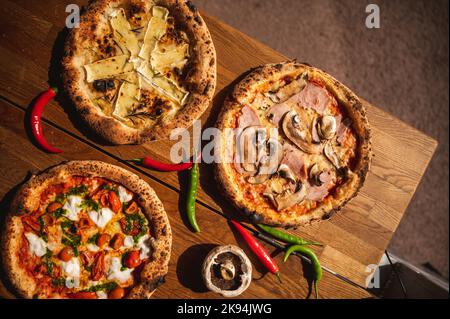 A top view of three types of pizza with chili peppers and mushroom on wooden board Stock Photo