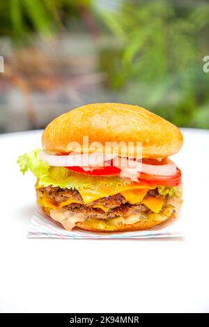 Double cheese american burger on a white table at a cafe with green background. Stock Photo