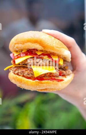 Hand holding cheese burger against a lush green background. Stock Photo