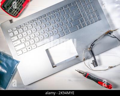 Repair and maintenance of computer laptop, laptop lid disassembled, and screwdriver hanging above. Stock Photo
