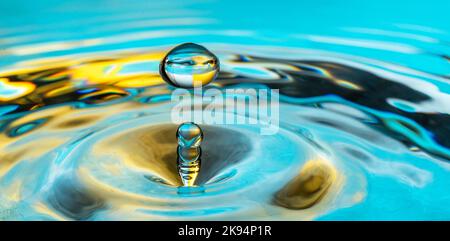 Water drop splash in a glass blue colored. Stock Photo