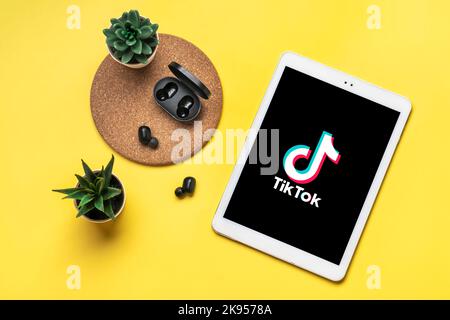 Bangkok, Thailand October 2022 Tablet Tik Tok application icon, logo on screen, wireless headphones, charger capsule on yellow table Trendy social media network concept Flat lay Top view. Stock Photo