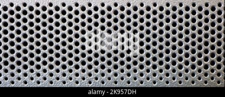 Grid in the form of round holes in a silvery plastic panel. Perforated surface with mesh pattern. Abstract background. Stock Photo