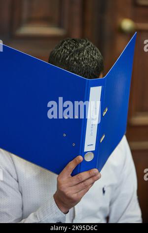 Hamburg, Germany. 26th Oct, 2022. The defendant sits in the courtroom before the trial begins, holding a blue file folder in front of his face. The 27-year-old is on trial for attempted manslaughter. The defendant is alleged to have fatally injured his partner with a knife in October 2021. He fled across adjacent rooftops and was arrested in Paris on November 11, 2021, on an international arrest warrant and transferred to Germany. Credit: Georg Wendt/dpa/Alamy Live News Stock Photo