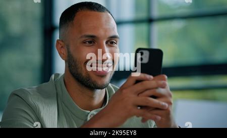 African American bearded man indoors using smartphone male employer entrepreneur businessman with phone sitting at office typing chatting with mobile Stock Photo