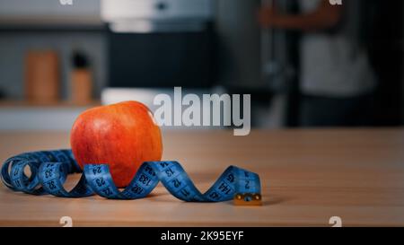 Red apple and tape measure on kitchen table unrecognizable blurred African man athlete opening fridge searching ingredients for lunch eating cooking Stock Photo