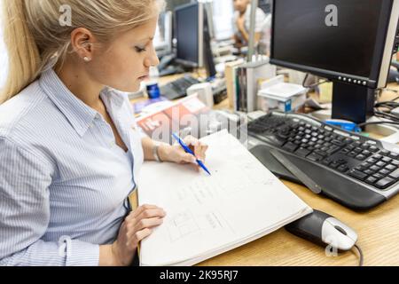 The Media Agency: Making Notes. A female media professional researching her next project at her desk in the office. From a series of related images. Stock Photo
