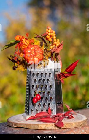 A four-sided grater has been decorated with autumn flowers, plants and leaves, on a bokeh background Stock Photo