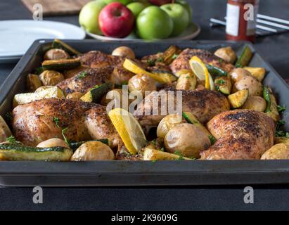 Roasted chicken legs with vegetables. Served hot on a baking tray on dinner table at home. Front view Stock Photo