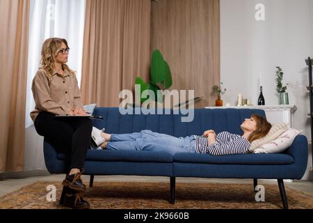 Depressed young caucasian woman lying on sofa during psychotherapy session Stock Photo